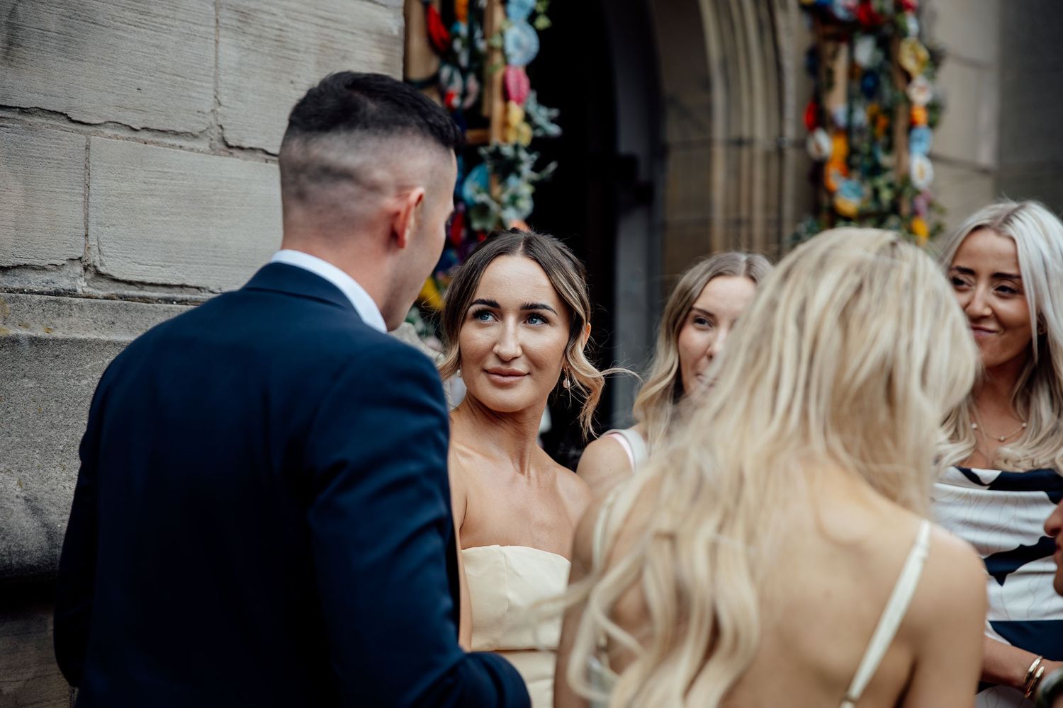 Wedding celebration outside historic stone building with colorful floral arch.