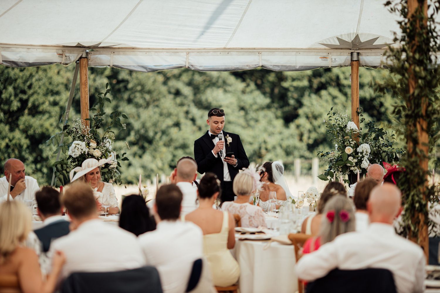 Wedding reception setup under a white tent with elegant table settings and floral decorations.