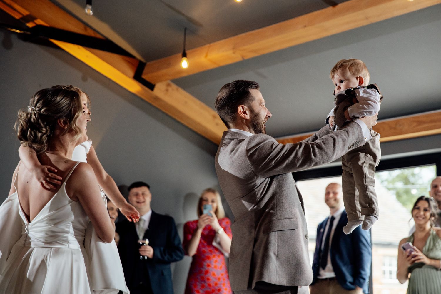 Wedding guests dancing and celebrating on a wooden floor during a reception.