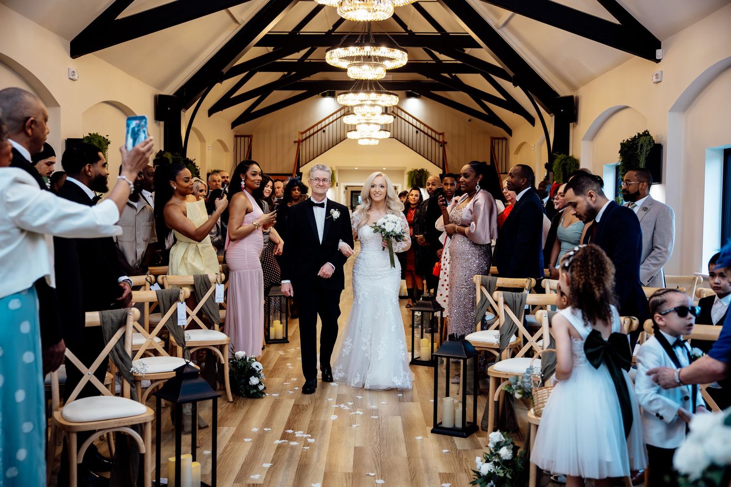 Bride walking down the aisle with her father in a stunning chapel filled with wedding guests.