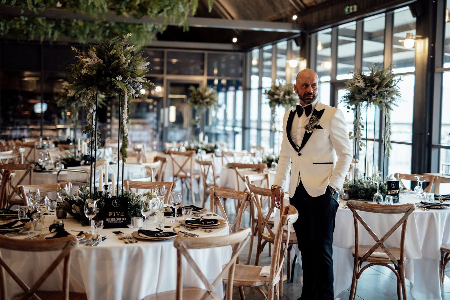 Elegant wedding reception venue with rustic wooden chairs and tables decorated with floral centerpieces.