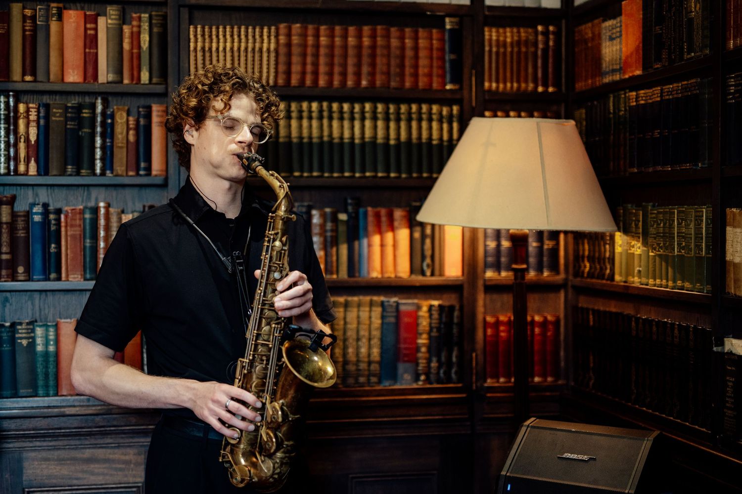 Saxophone player performs in front of vintage library bookshelves.