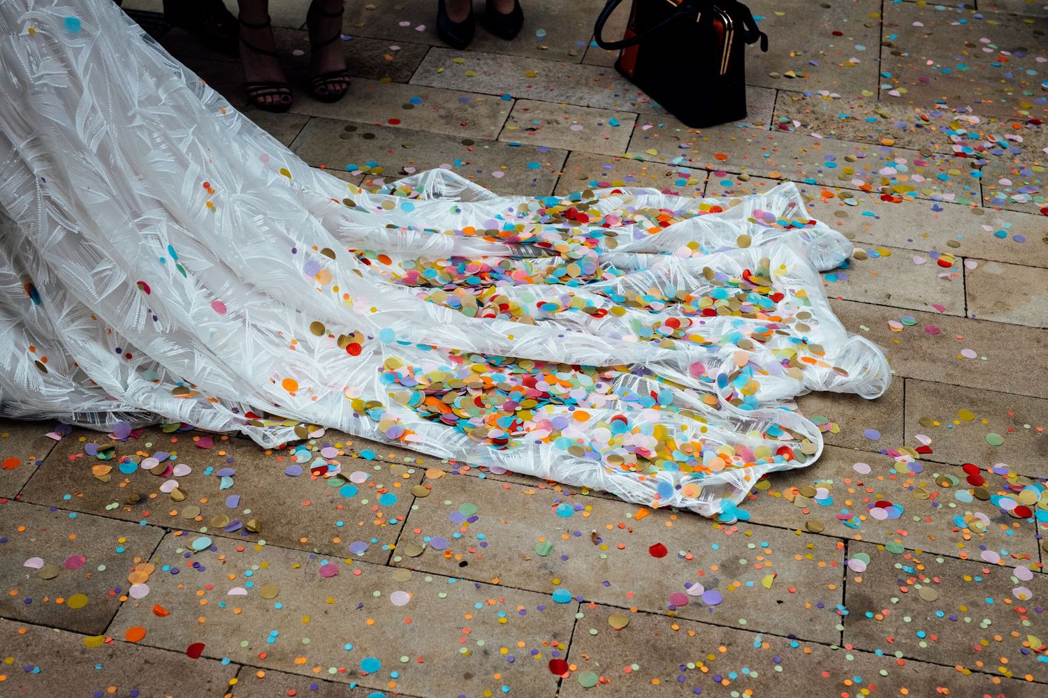 White wedding dress train surrounded by colorful confetti on stone floor.