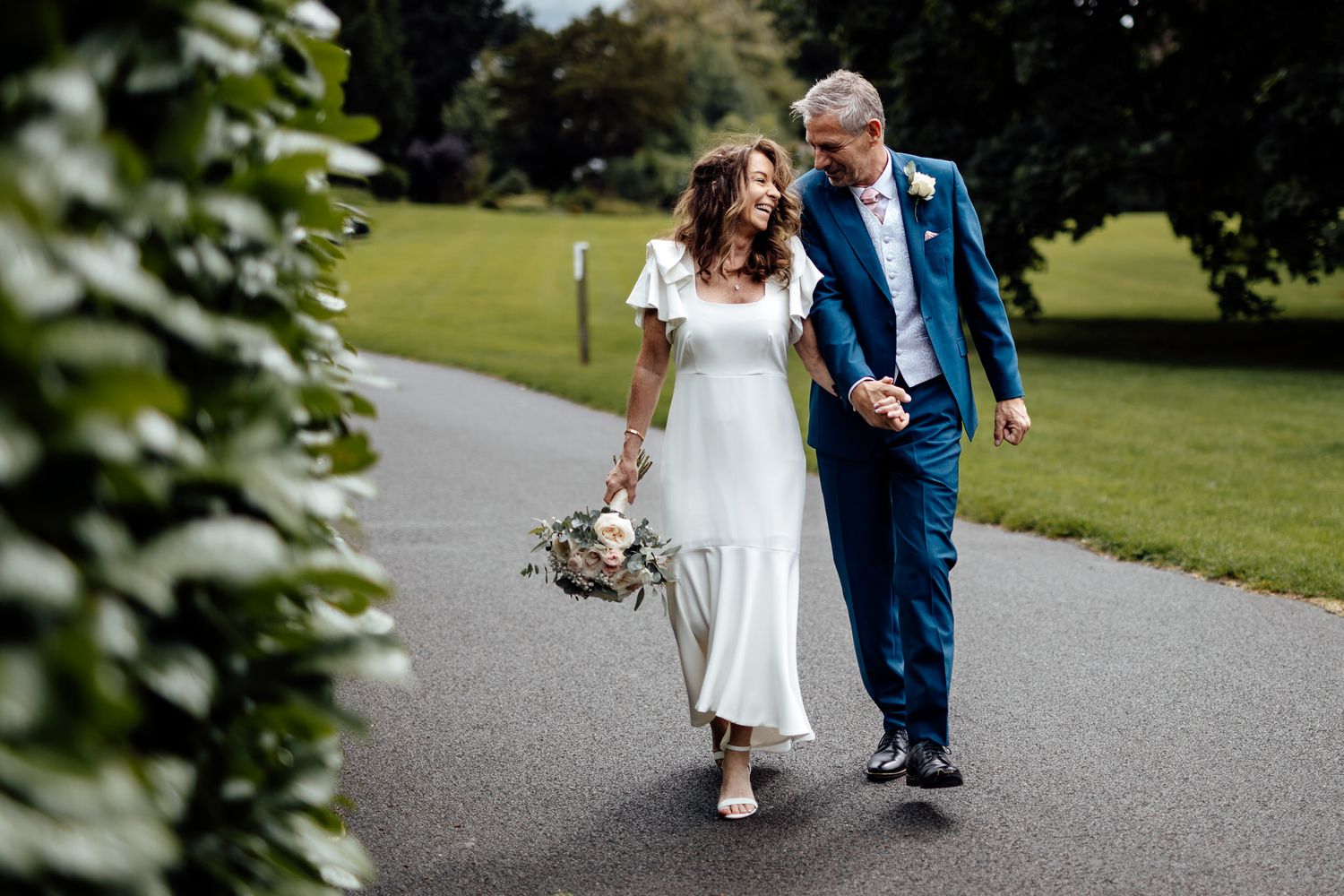 Couple strolling along garden pathway surrounded by greenery.