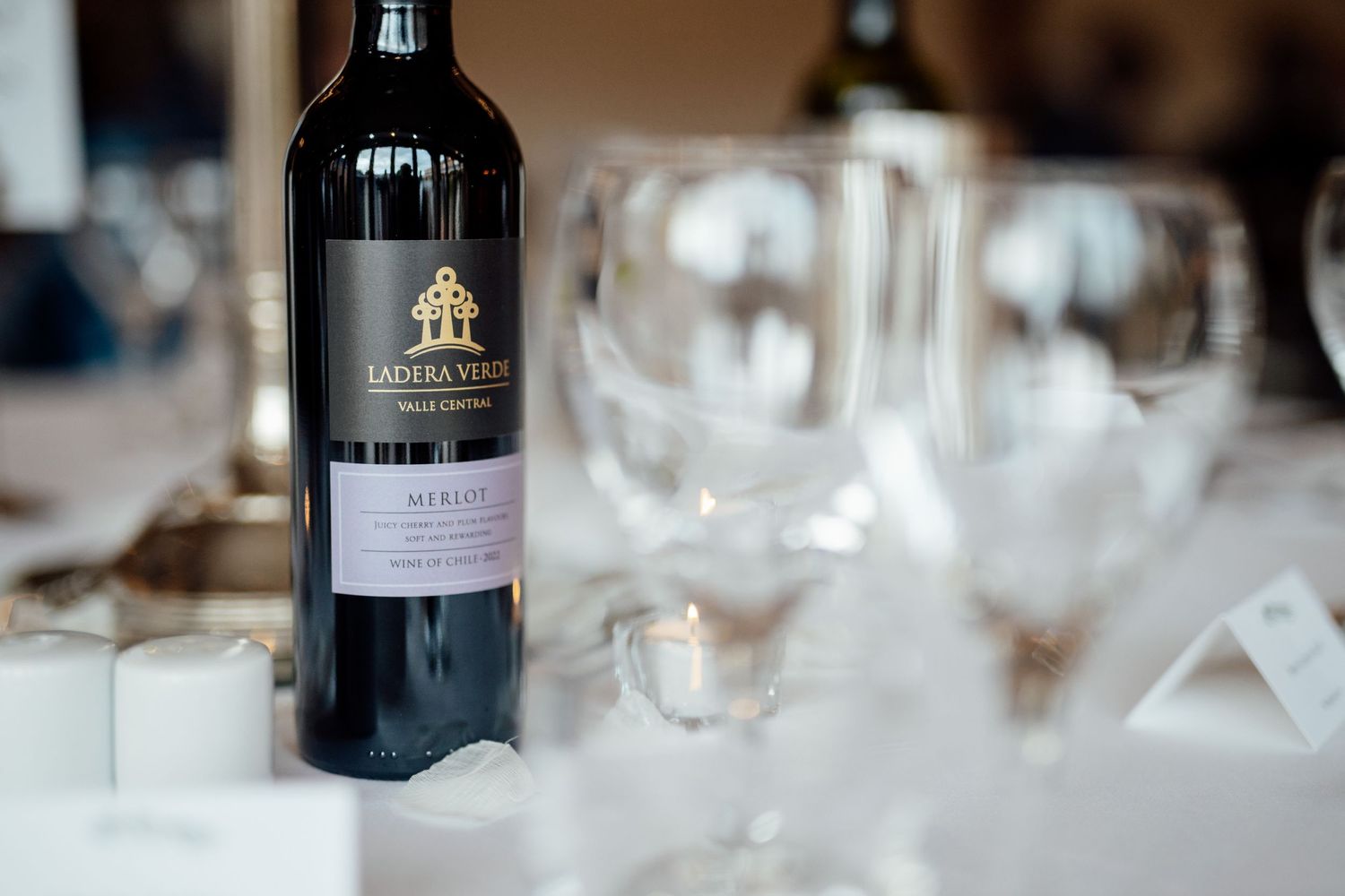 Row of wine bottles and glasses set on formal dining table.