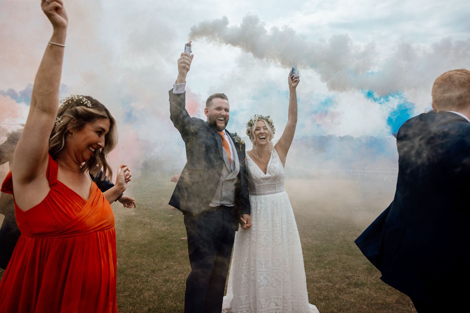 Wedding guests dance and celebrate with smoke effects during an outdoor reception celebration.