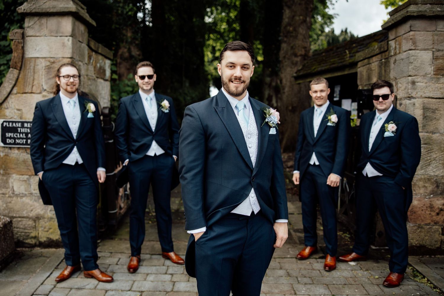 Groomsmen in navy suits posing against stone wall backdrop.