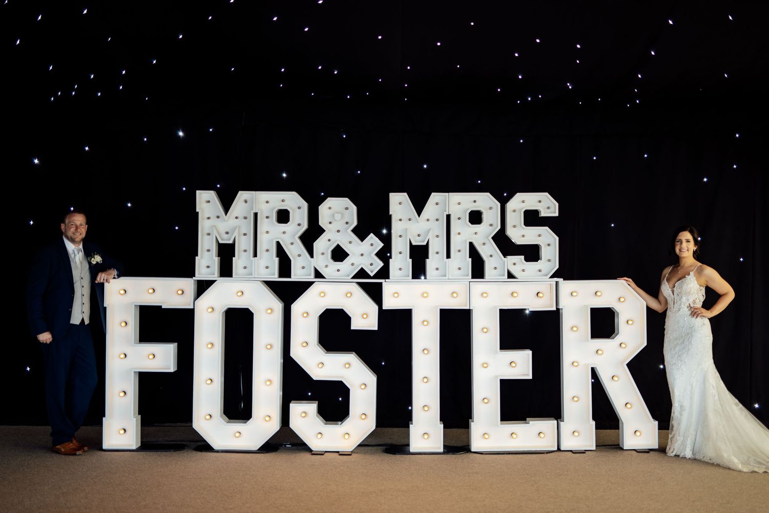 Illuminated 'MR & MRS FOSTER' sign against starry night backdrop at wedding reception.