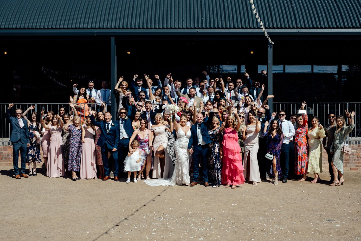 Large group photo of wedding guests lined up outside rustic venue.