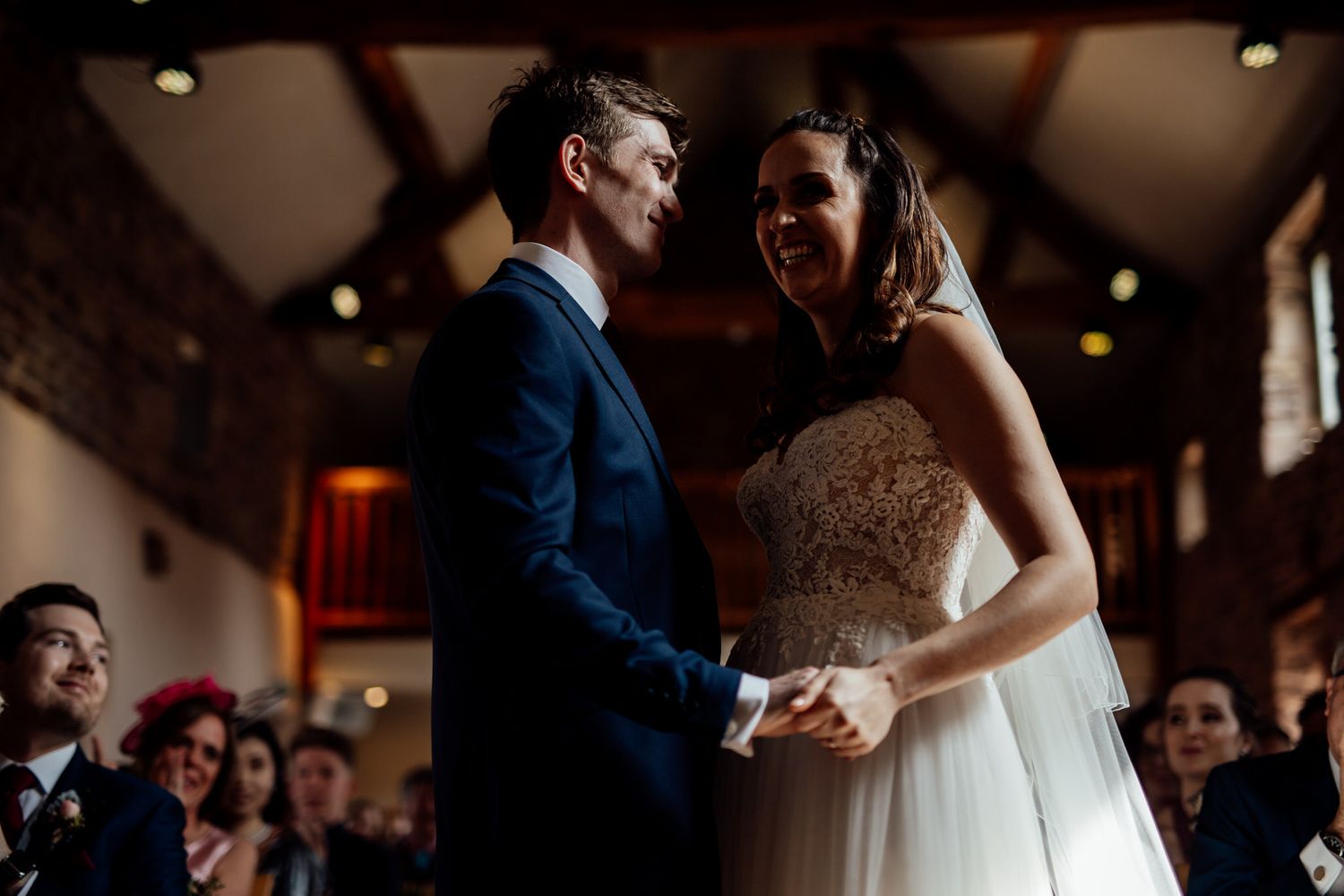 Wedding couple sharing their first dance in a rustic venue with wooden beams and warm lighting.