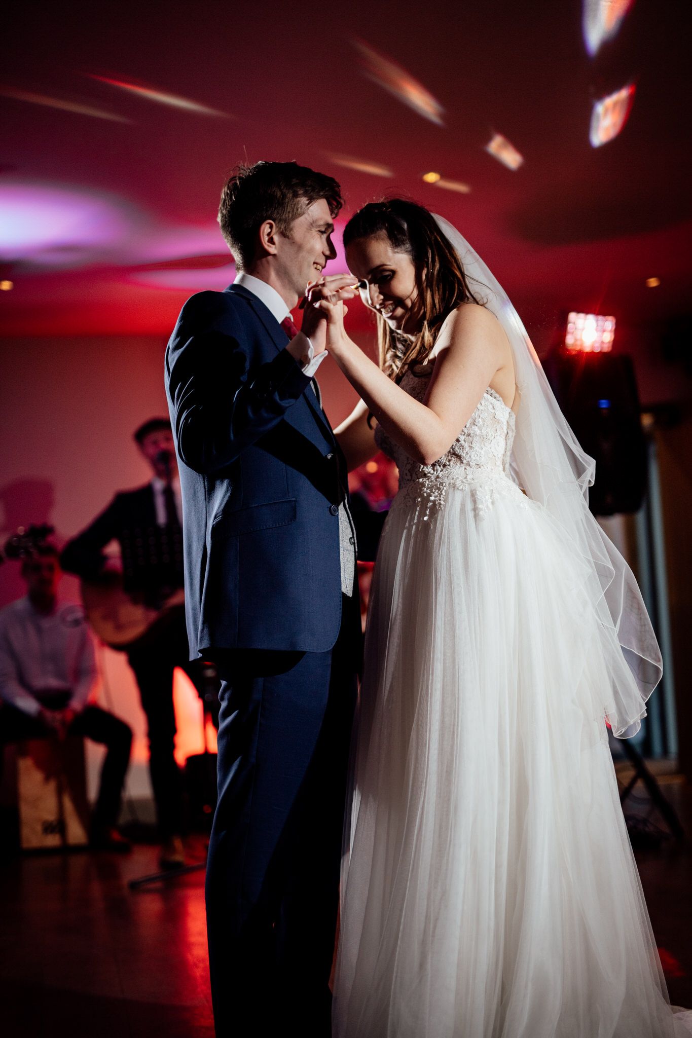 Couples dance together in a dimly lit reception venue with romantic red lighting.