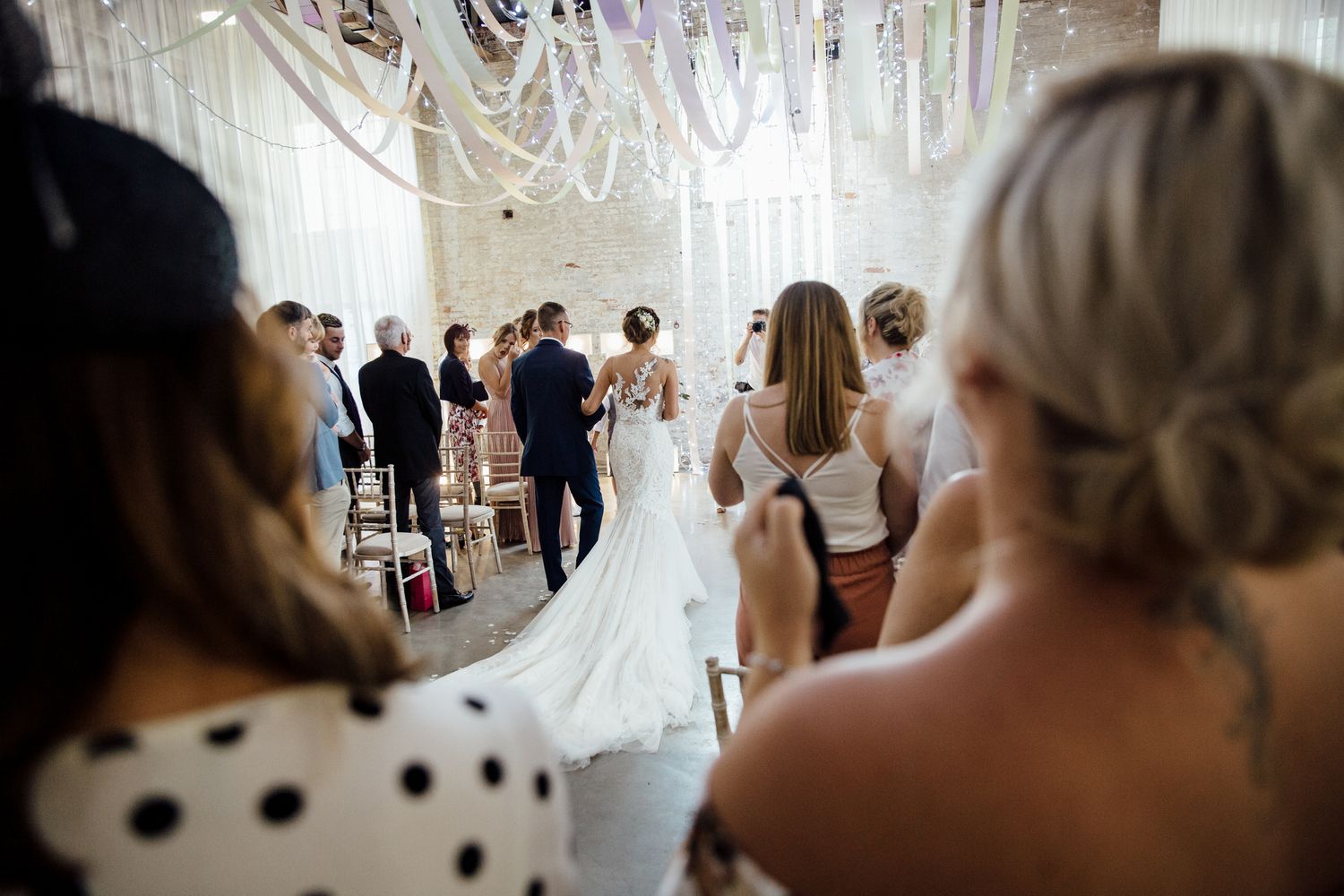 Wedding guests watching ceremony through decorative hanging ribbons and lights.