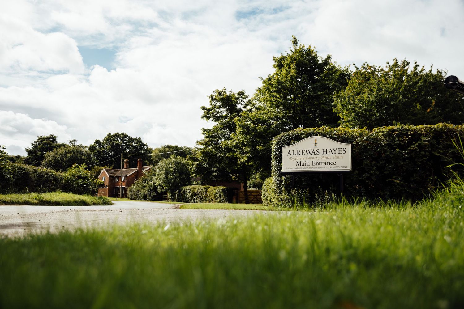 Entrance sign to a venue surrounded by lush green grass and trees.