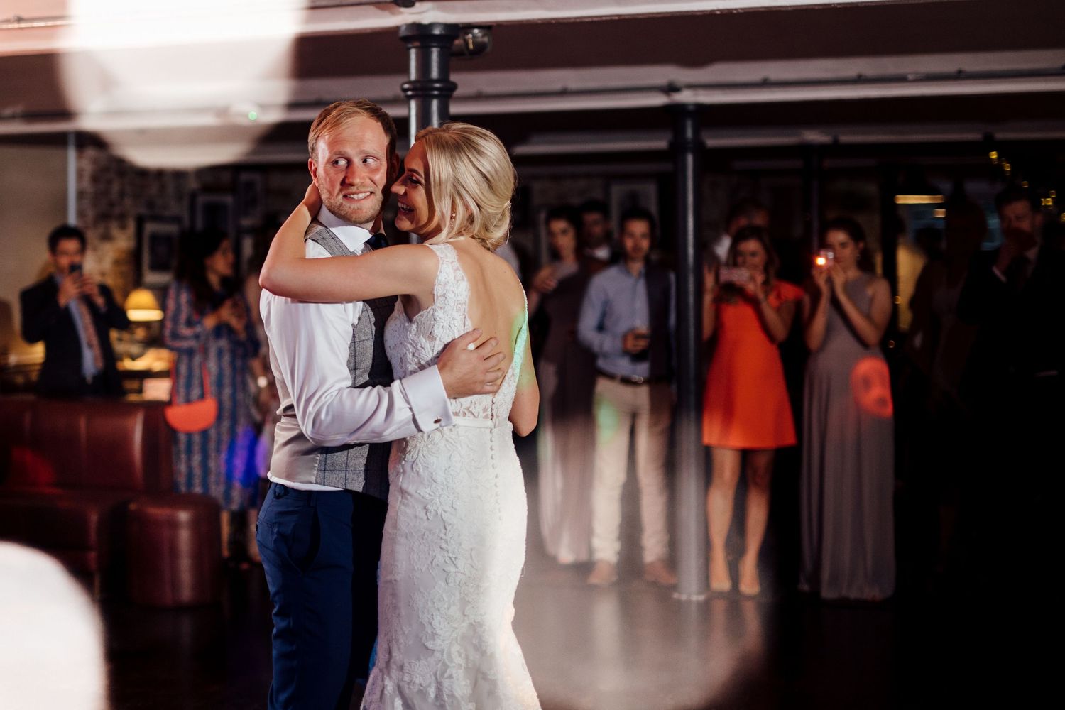 Newlyweds share their first dance while wedding guests look on from the background.