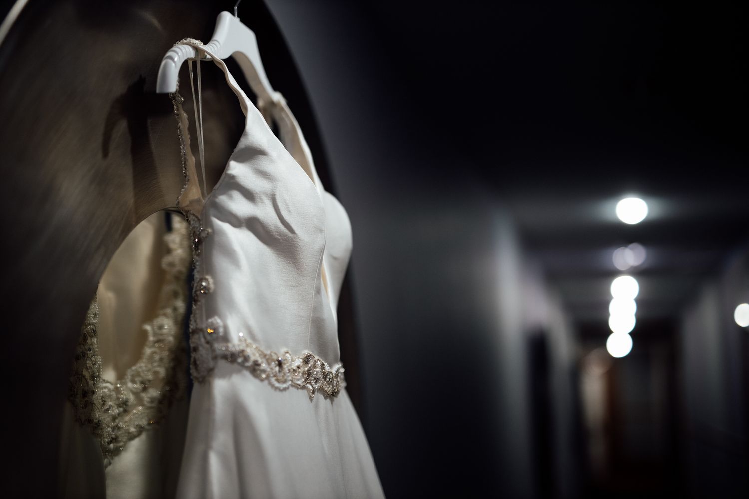 Elegant white wedding dress with intricate beading displayed against a dark background.