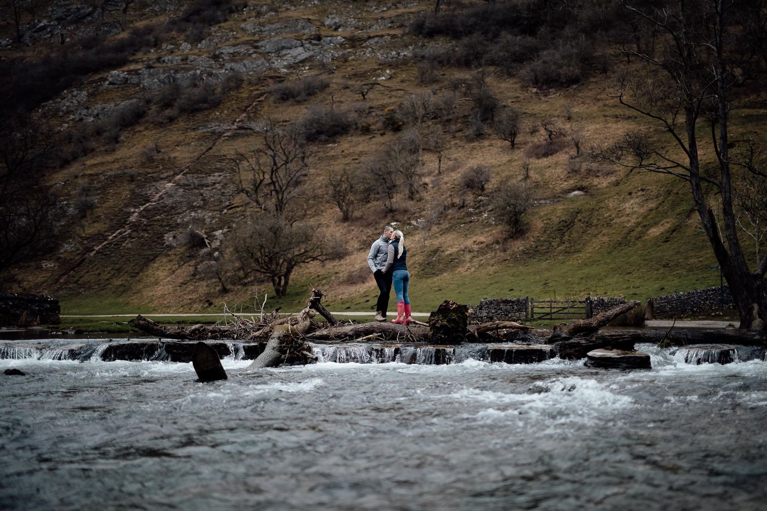 A rushing river flows beneath a wooden bridge in a rugged mountainous landscape.