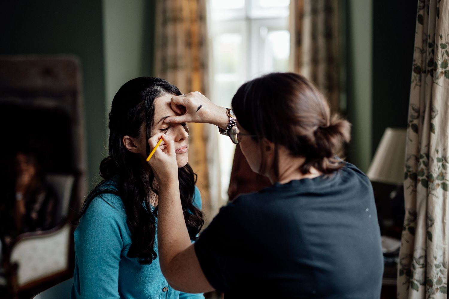 Makeup artist applying cosmetics in a room with natural window light.