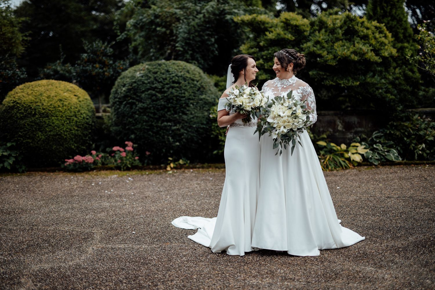 Two people in white dresses sitting together in a beautiful garden landscape.
