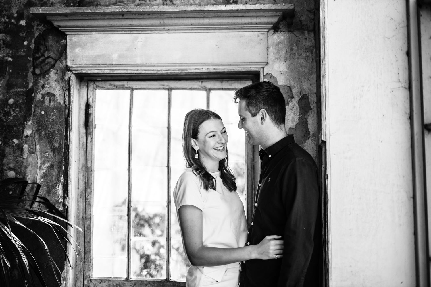 A black and white series of intimate moments captured near a bright window in an industrial space.