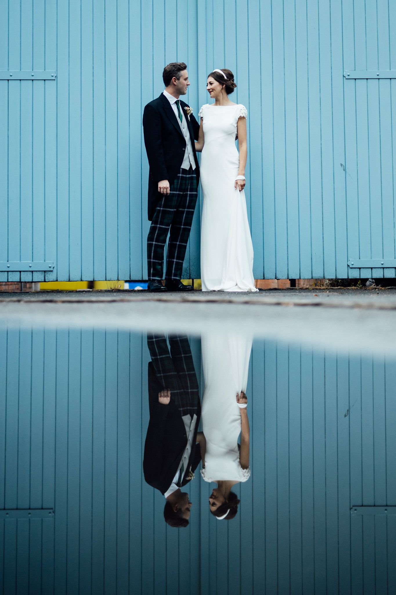 Wedding couple reflected in water against a blue wall creating an artistic mirror effect.