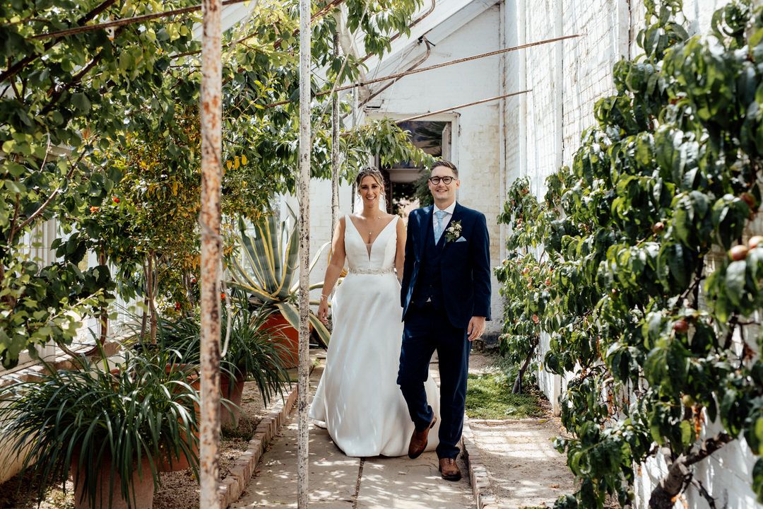 Wedding couple photographed in greenhouse setting surrounded by tropical plants and natural light.