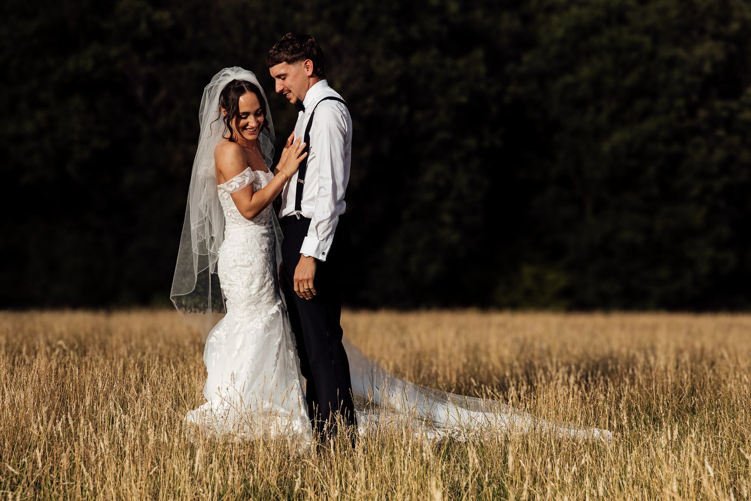 Romantic couple embracing in sunlit field wearing wedding attire.