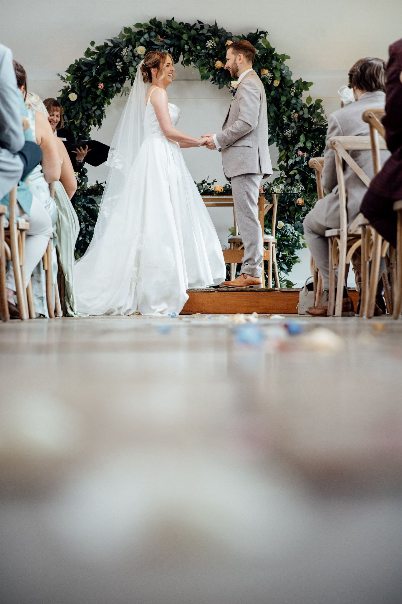 A wedding ceremony under a lush greenery arch with guests seated in wooden chairs.