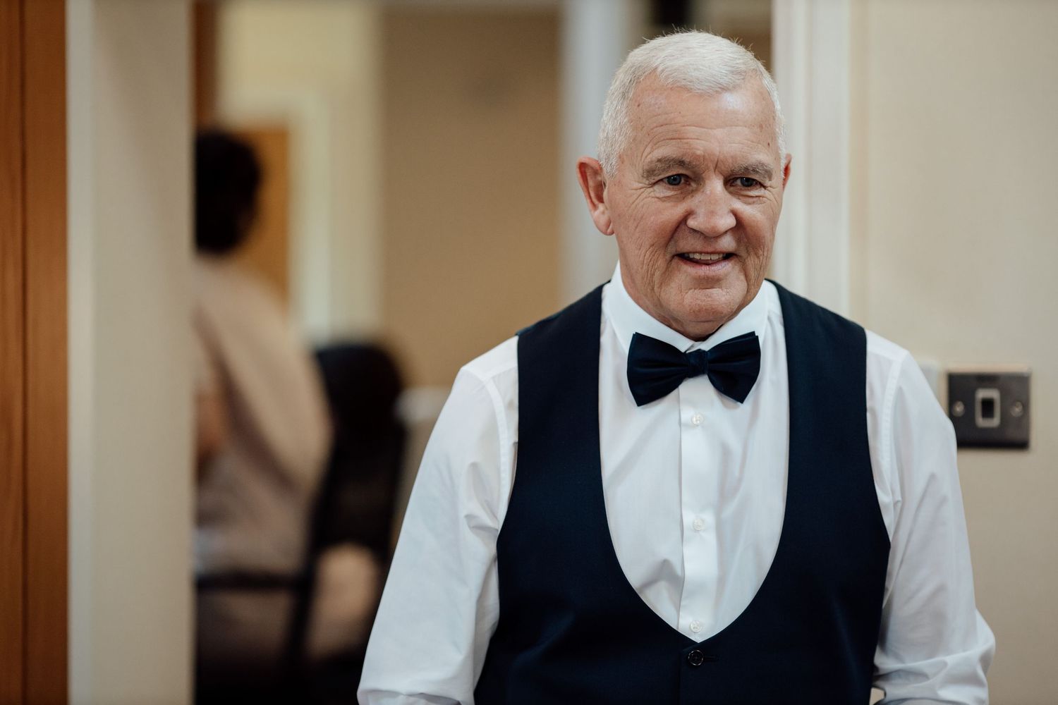 Man in formal attire adjusts his bowtie while getting ready for special occasion.