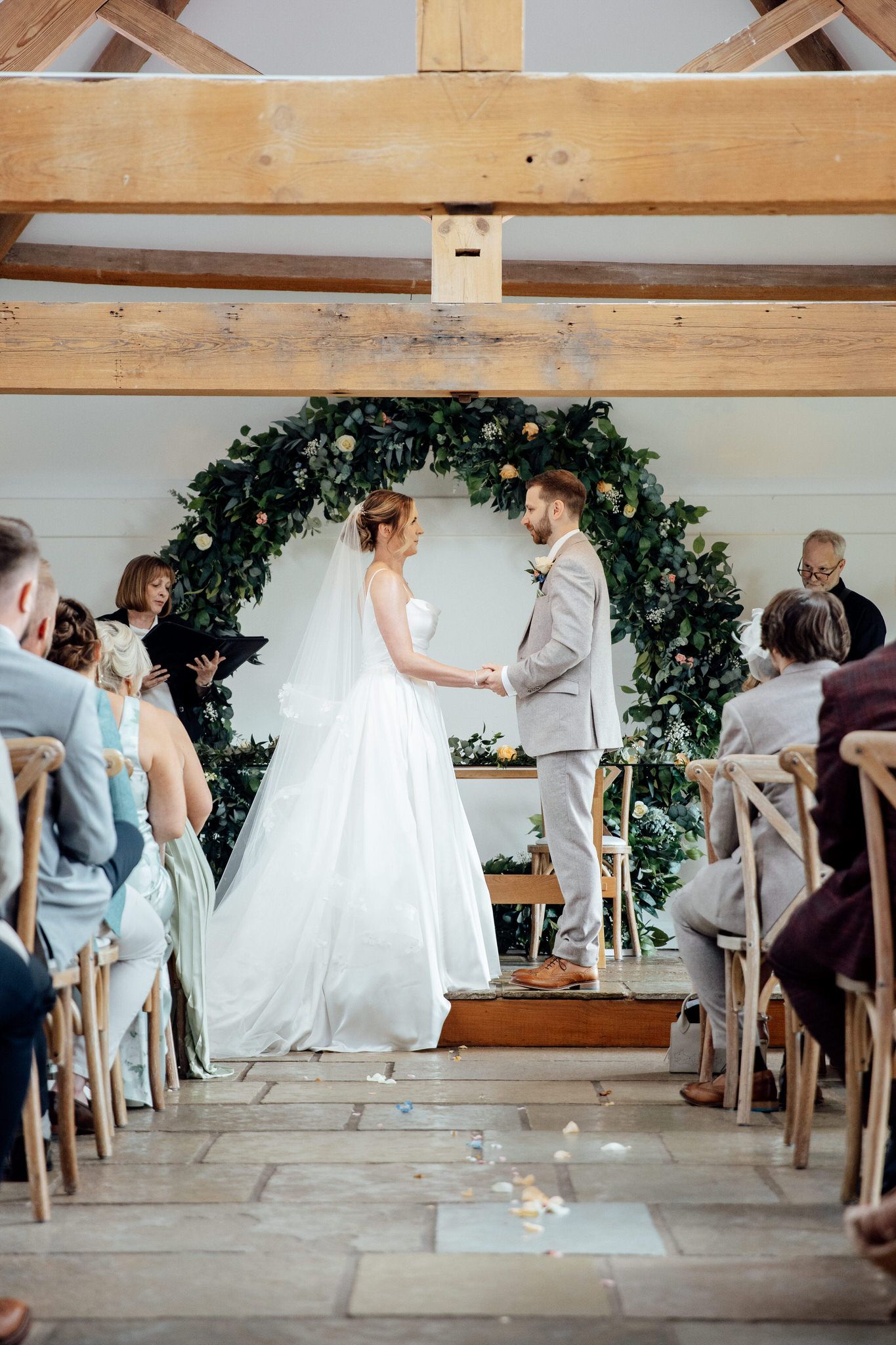 Wedding ceremony setup in a rustic wooden barn with greenery decorations and guests seated.
