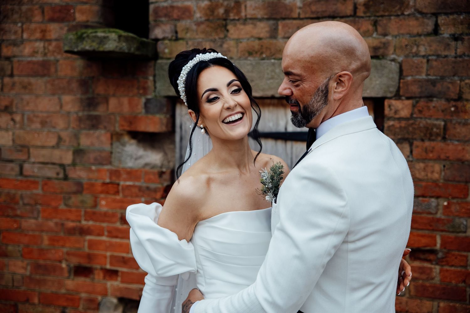 Romantic wedding moment captured against rustic brick wall backdrop.