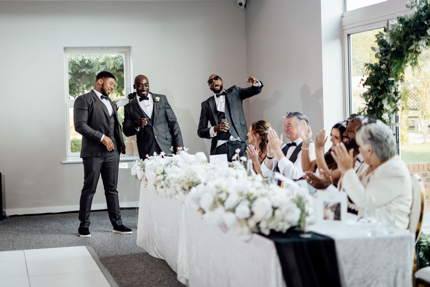 Elegant white wedding reception setup with floral centerpieces in a bright indoor venue.