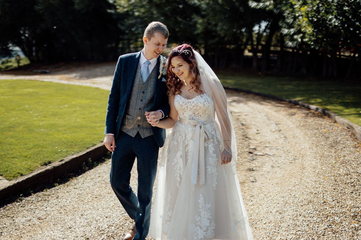 Couple walking along a gravel path surrounded by lush greenery on their wedding day.