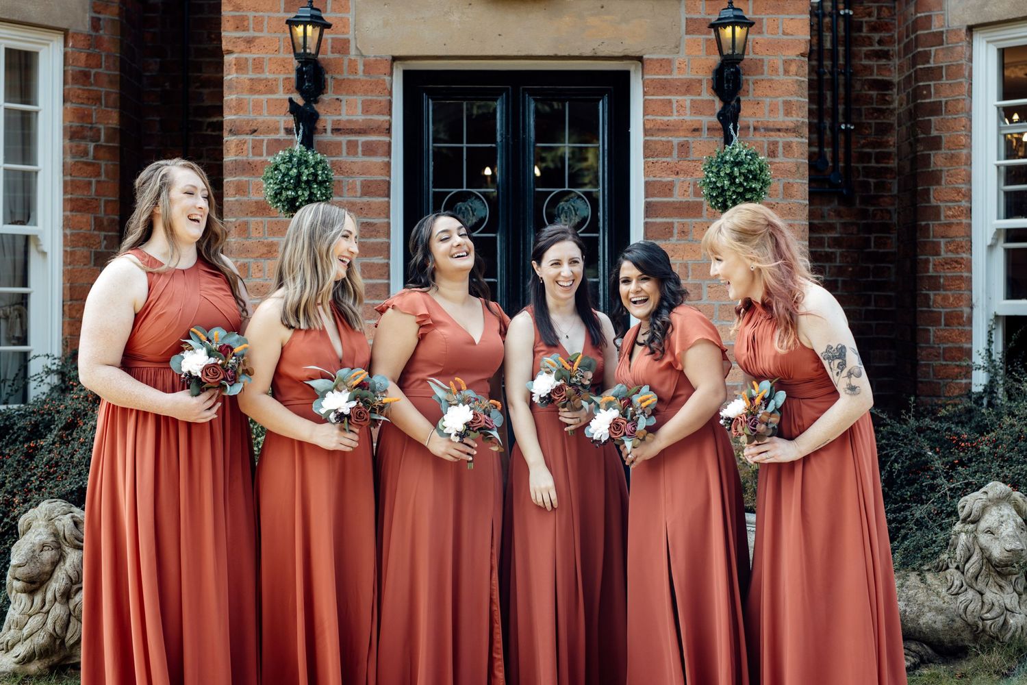 Group wearing matching coral-colored dresses standing in a row against a brick building exterior.