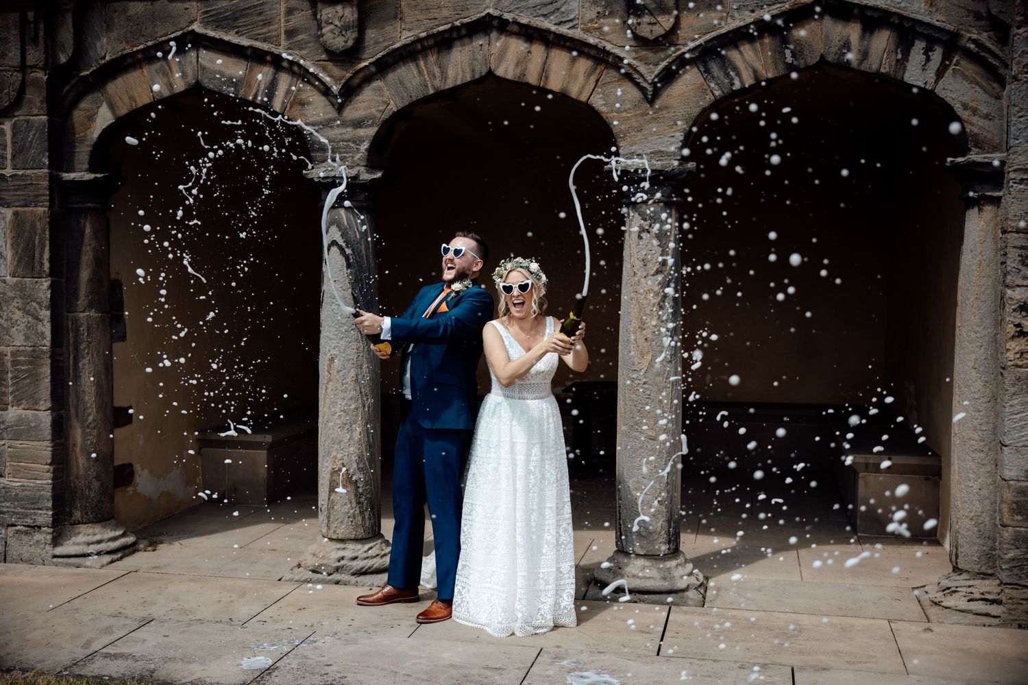Newlyweds celebrate under shower of confetti at stone archway entrance.