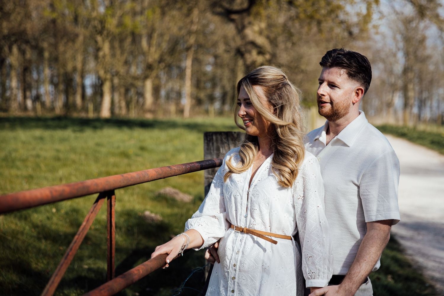 A couple shares tender moments while walking along a rustic fence-lined path.