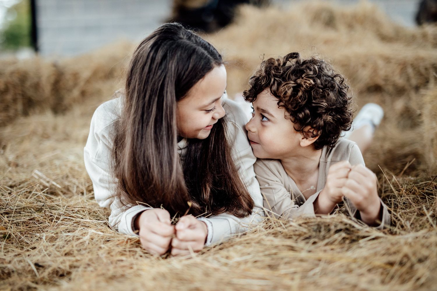 A couple lies together in golden hay, sharing intimate moments during a photo session.