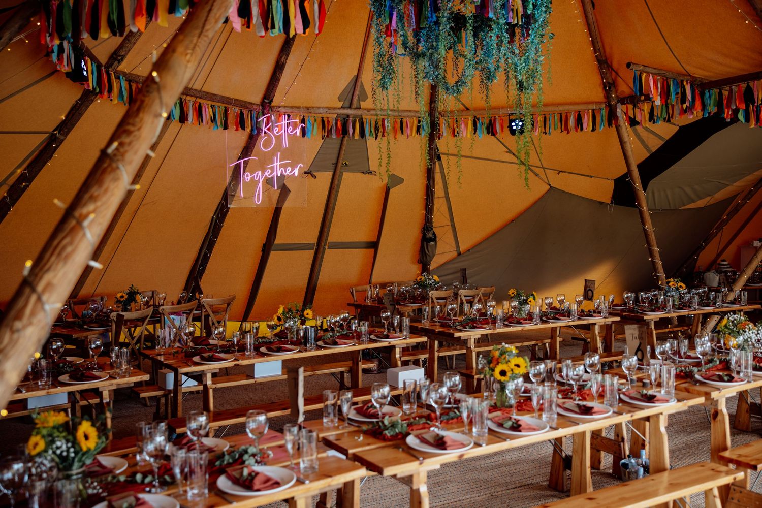 Interior view of a decorated tipi wedding venue with rustic tables and colorful bunting.