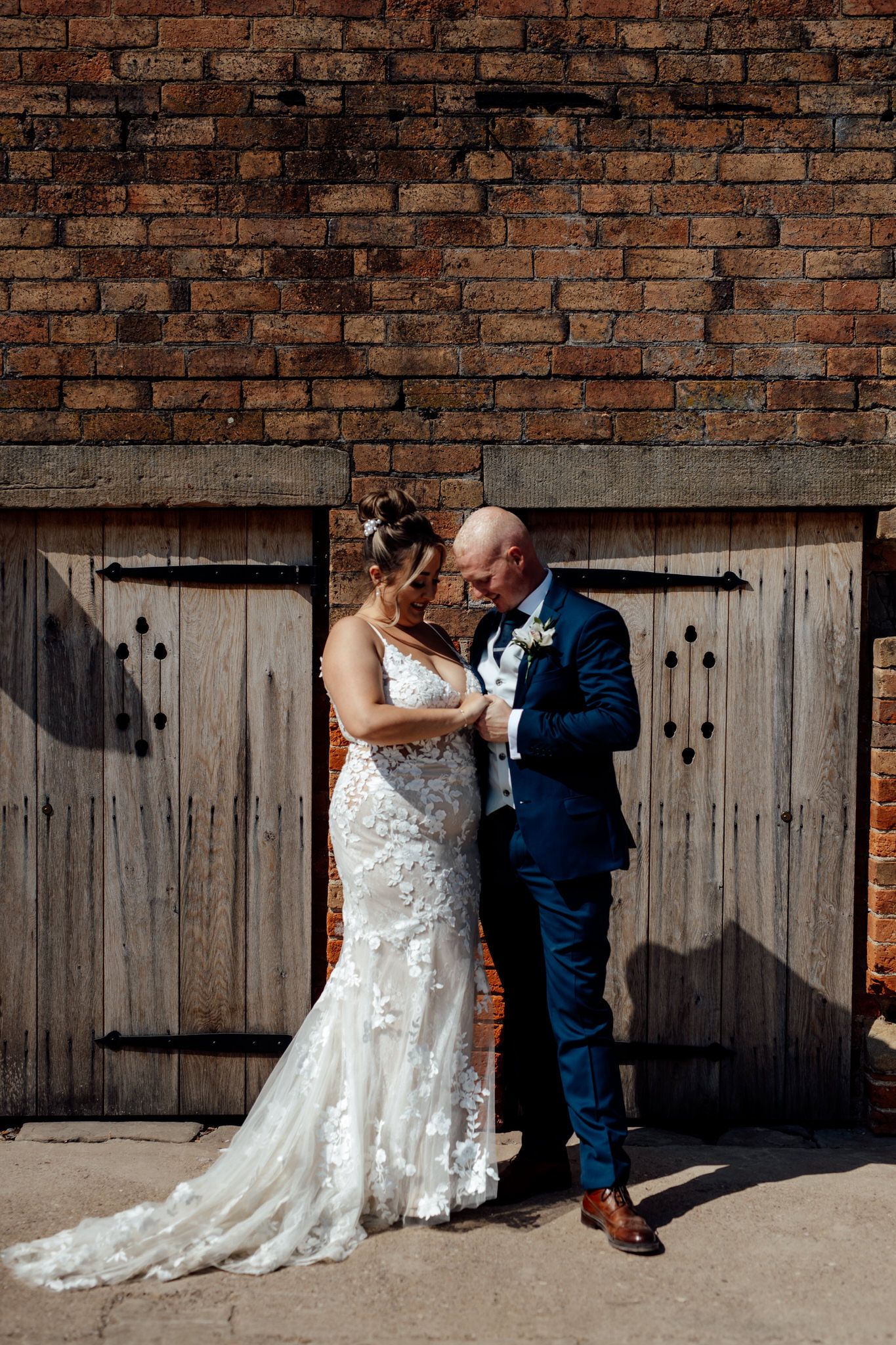 Wedding couple posing against rustic wooden doors and brick wall backdrop.
