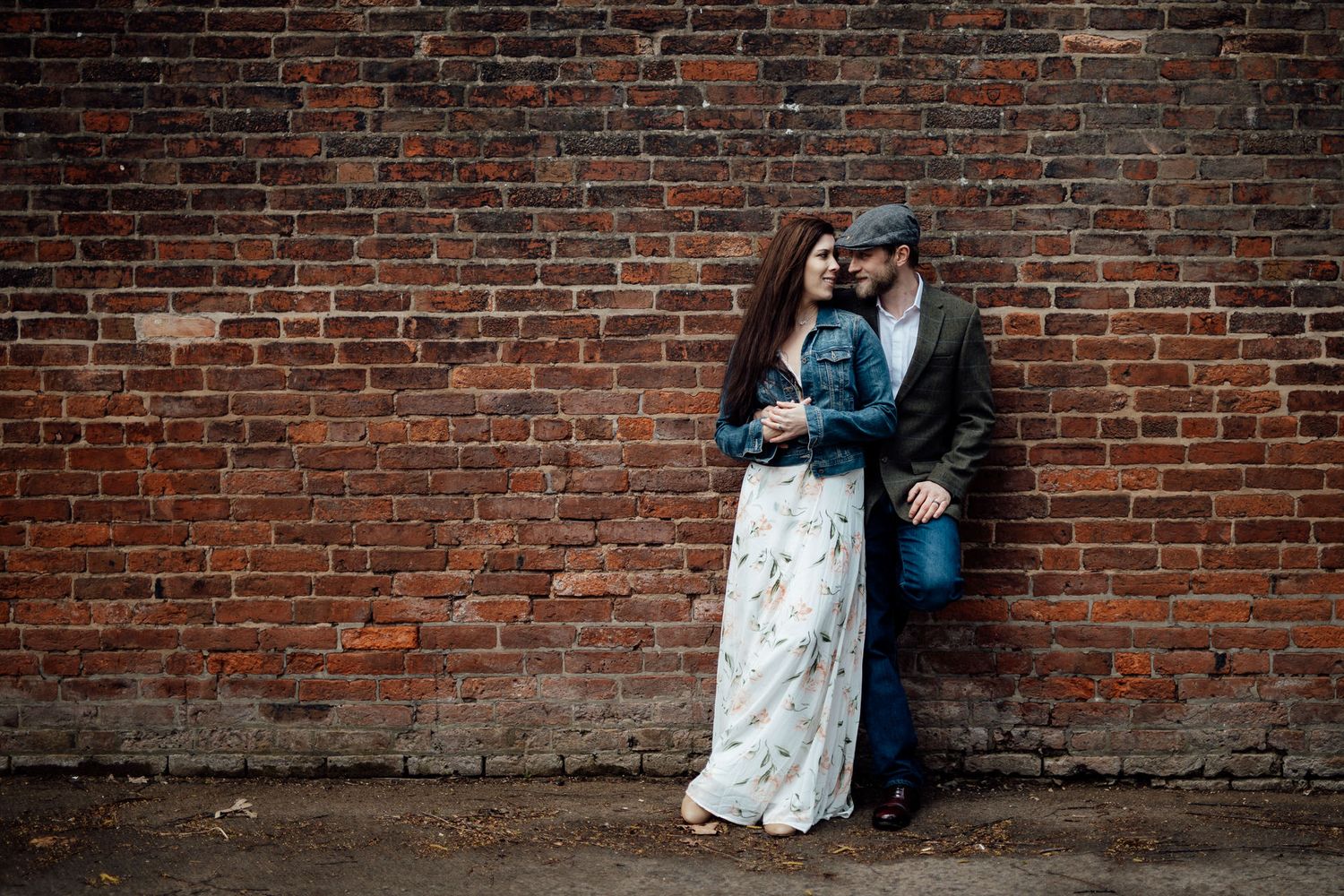 A couple embraces against a rustic brick wall, creating a romantic urban portrait.