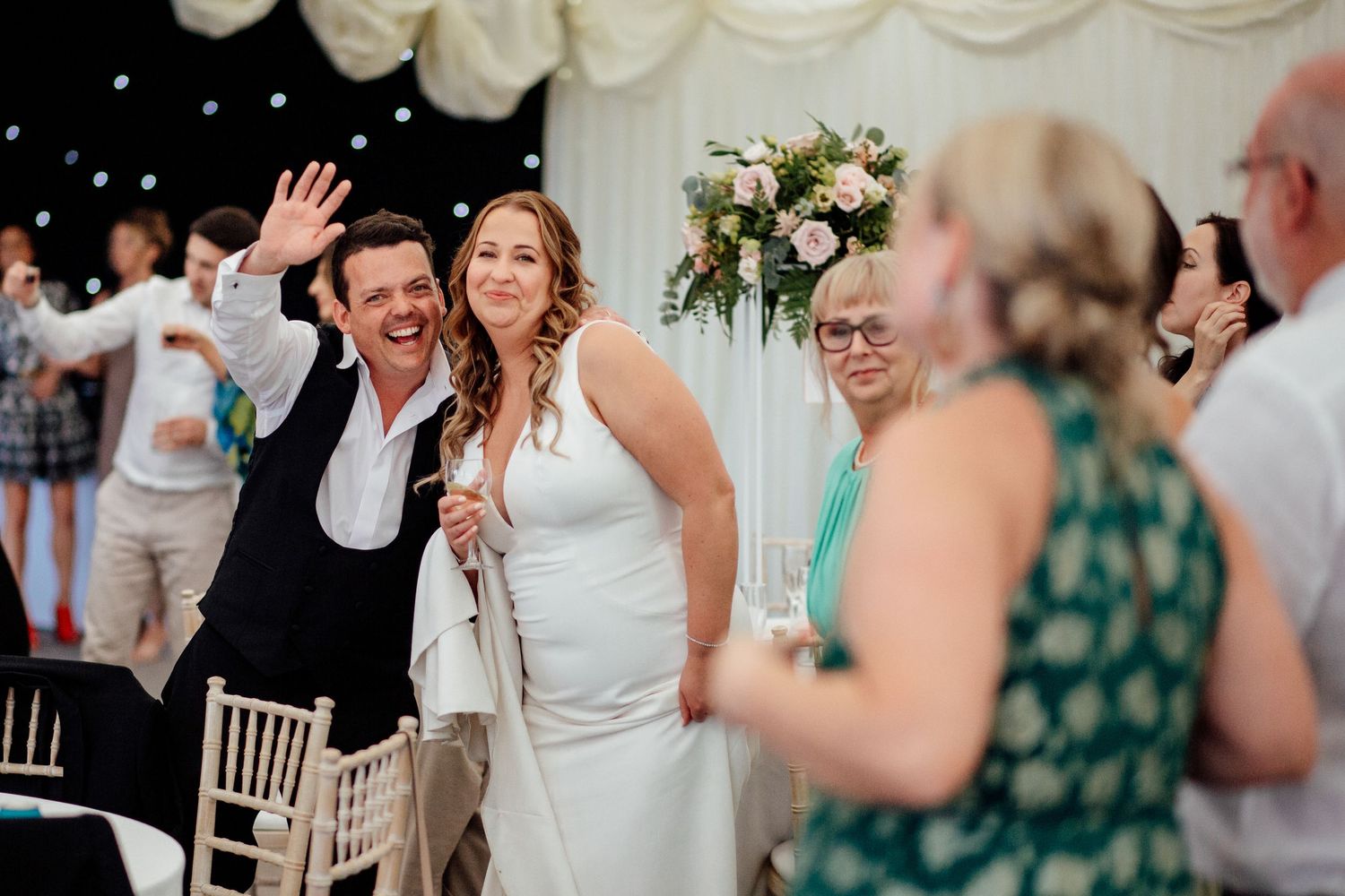 Joyful celebration moment at indoor wedding reception with white draping and floral decor.