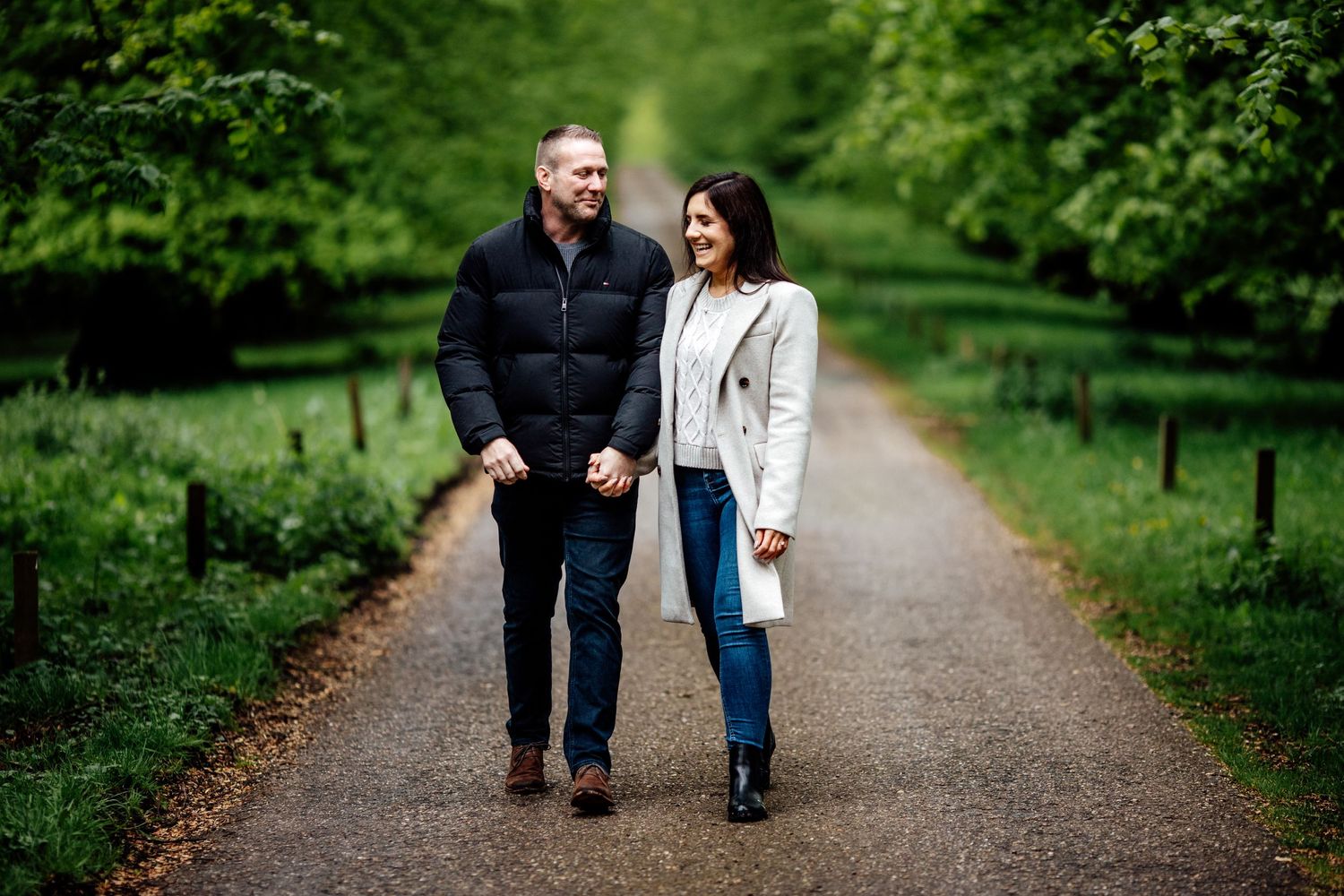 A couple walks together along a peaceful park pathway surrounded by greenery.