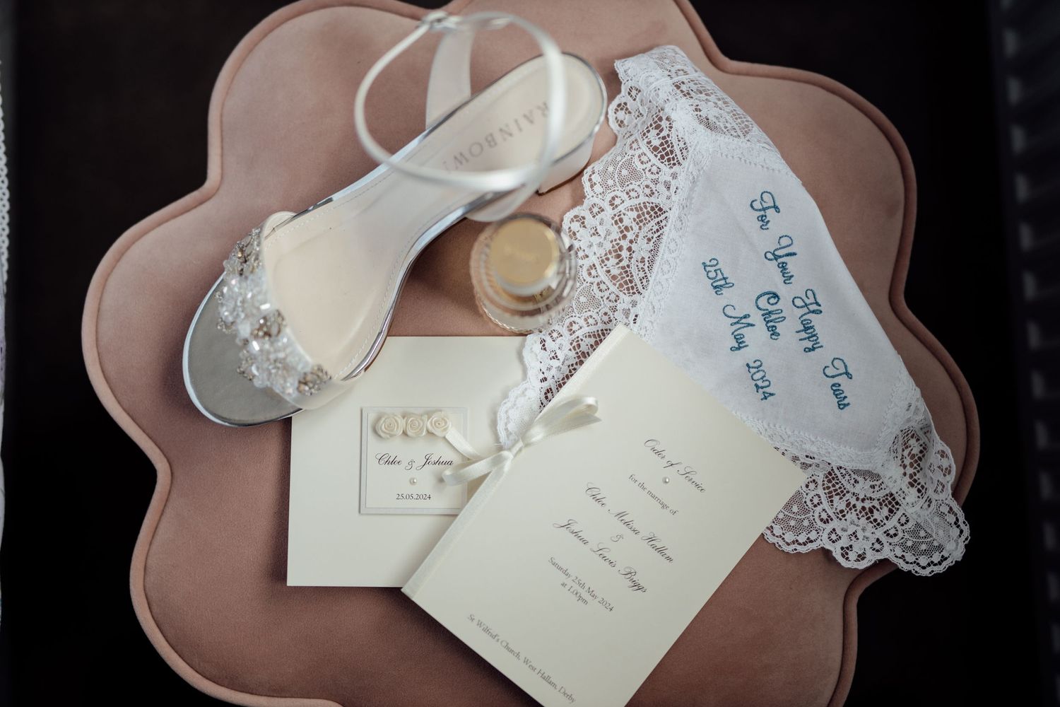 Wedding accessories including lace garter, invitation and bridal shoe arranged on pink scalloped plate.