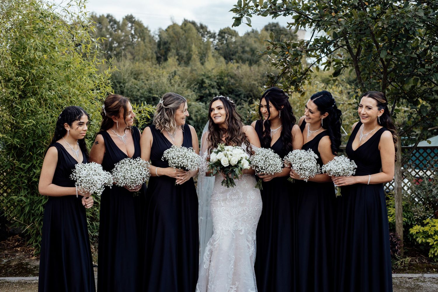 Bridesmaids in navy dresses pose with bride holding bouquets outdoors.