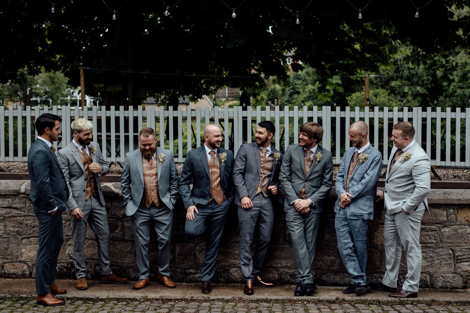 Wedding party posing casually on stone wall in coordinated gray attire.