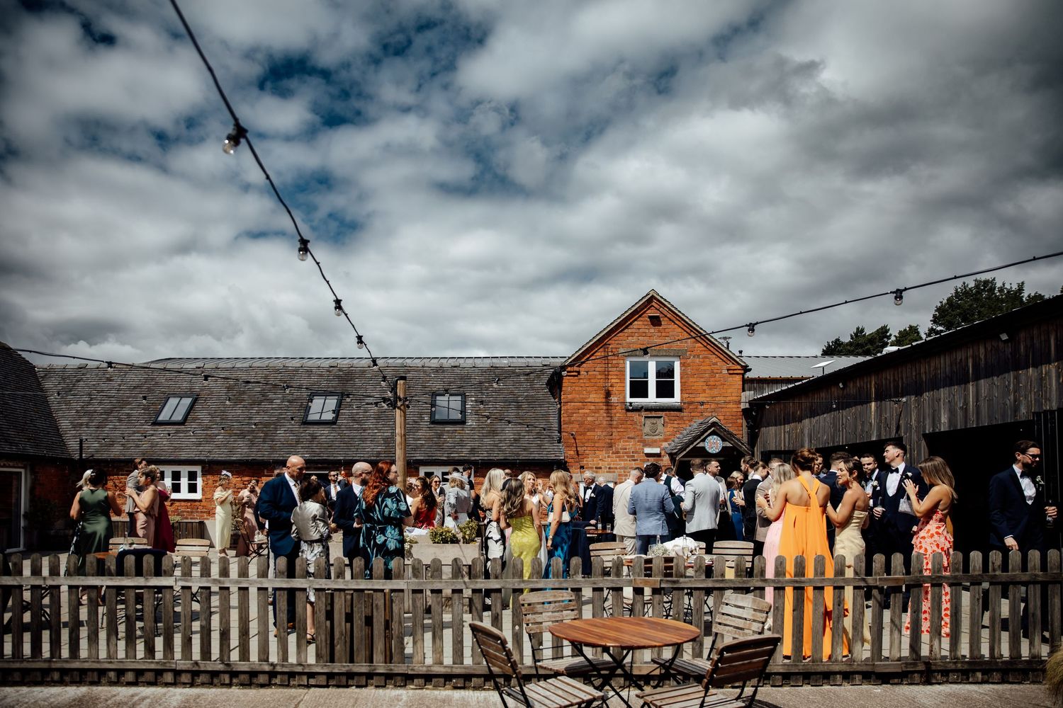 Panoramic view of wedding guests celebrating outdoors at a rustic brick venue.