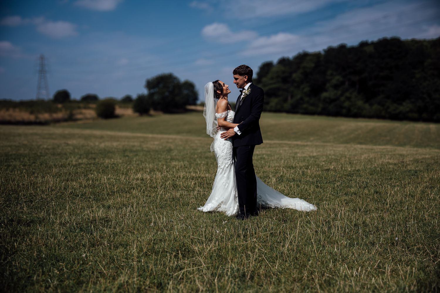 Couple in wedding attire standing together in sunlit meadow.