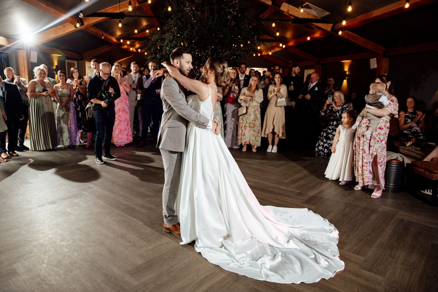 Wedding guests dance on a dark wooden dance floor during an evening reception celebration.