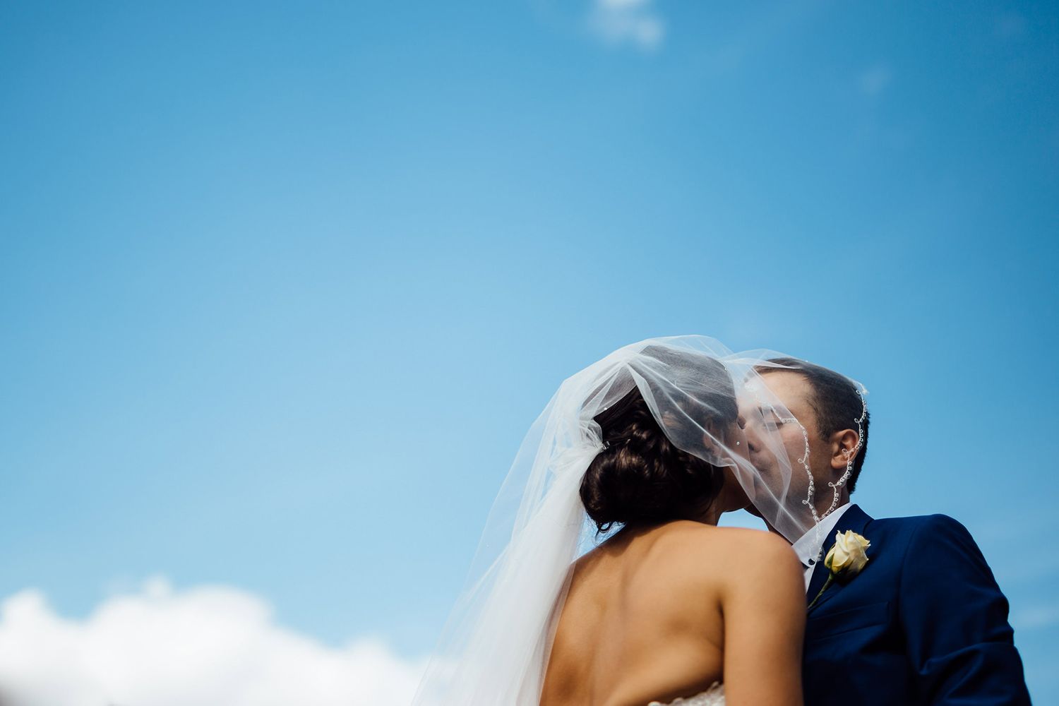 A romantic moment between newlyweds against a bright blue sky.