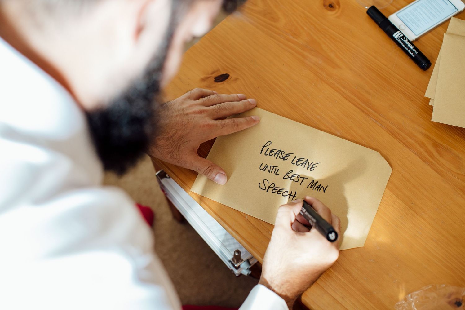 Hands writing notes and messages on wooden table during wedding preparations.