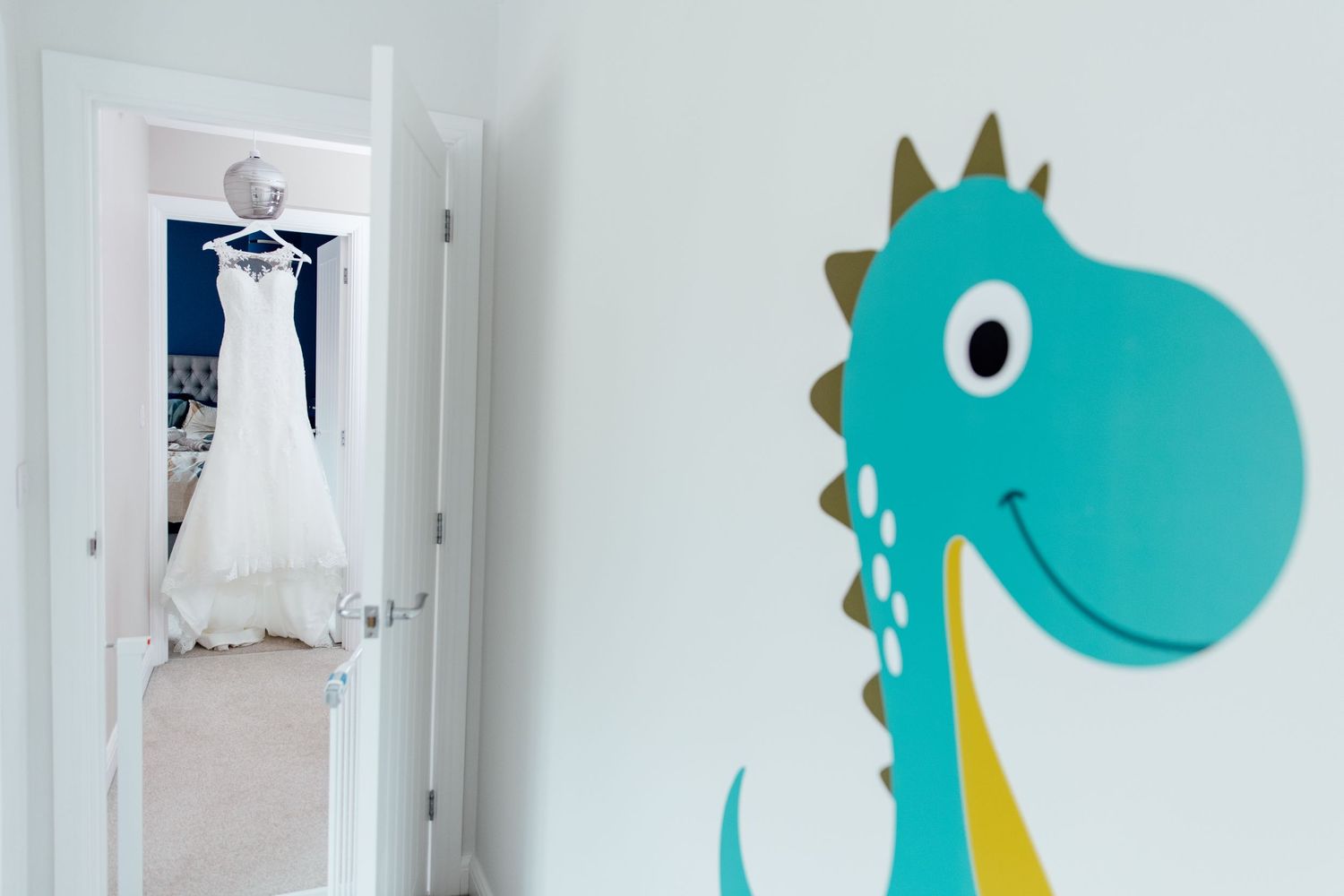 Whimsical turquoise dinosaur artwork decorates a white wall in a nursery setting.